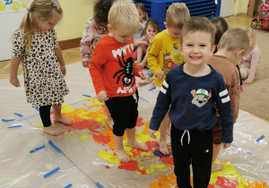 dzieci rozprowadzają farbę stopami po dużym kartonie