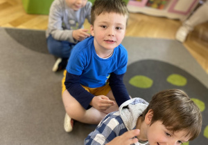 dzieci siedzą na dywanie i wykują masaż na plecach