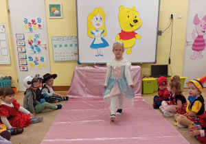 dziecko demonstruje strój idąc po różowym dywanie