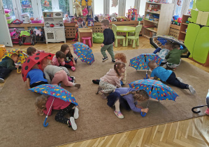 dzieci bawią się na dywanie z parasolkami
