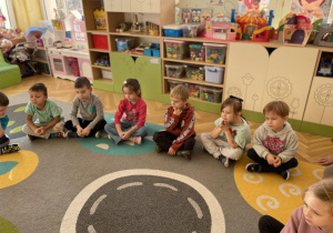 dzieci siedzą na dywanie i słuchają bajki czytanej przez mamę dziecka