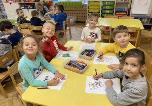 dzieci siedzą przy stole i rysują