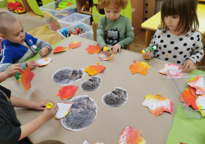 dzieci przyklejają jeże i liście tworząc pracę plastyczną