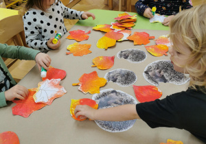 dzieci przyklejają jeże i liście tworząc pracę plastyczną