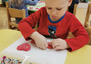 Dzieci robią serca z masy solnej i dekorują je koralikami.